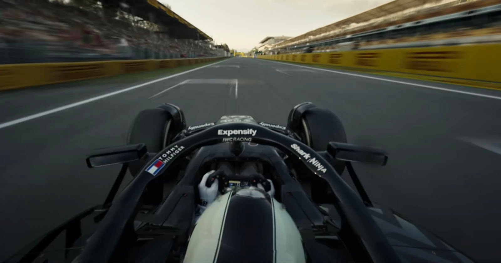 A view from behind the driver of a Formula 1 car racing down a straight track, with blurred grandstands and barriers on both sides, capturing a sense of speed and motion.