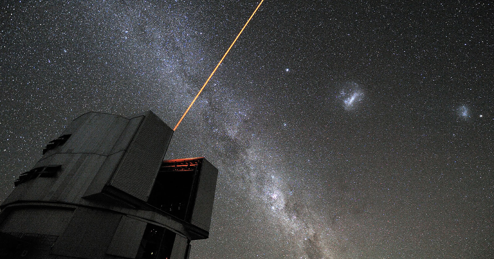 A large observatory telescope emits a bright orange laser into a star-filled night sky. The Milky Way galaxy is visible, with numerous stars scattered across the background.