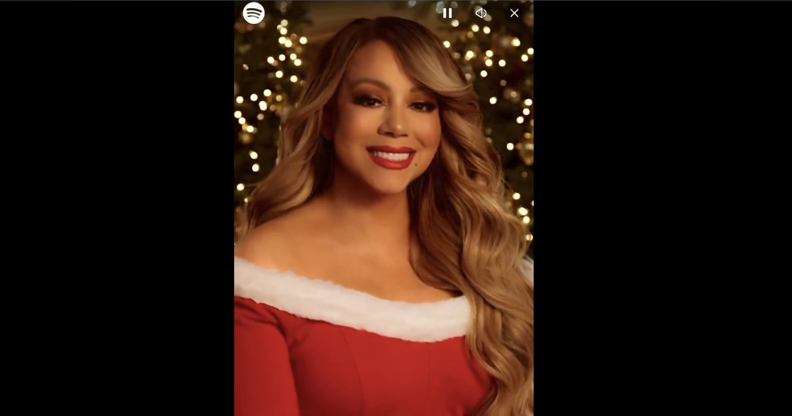 A person wearing a red dress with white trim, smiling in front of a background decorated with Christmas lights.