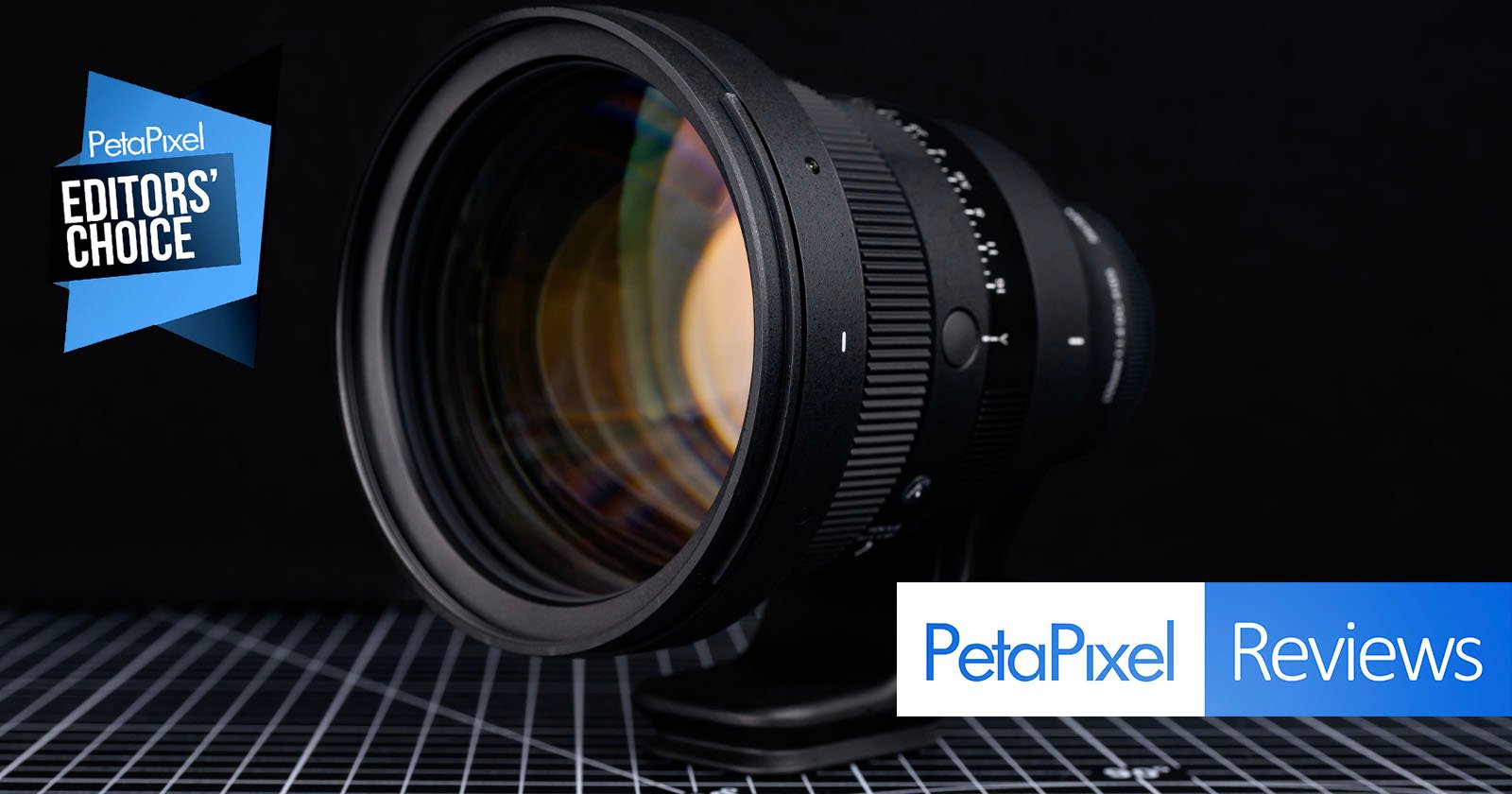 A camera lens is displayed on a checkered surface with a Petapixel Editors' Choice badge and Petapixel Reviews text in the bottom right corner. The background is dark and out of focus.