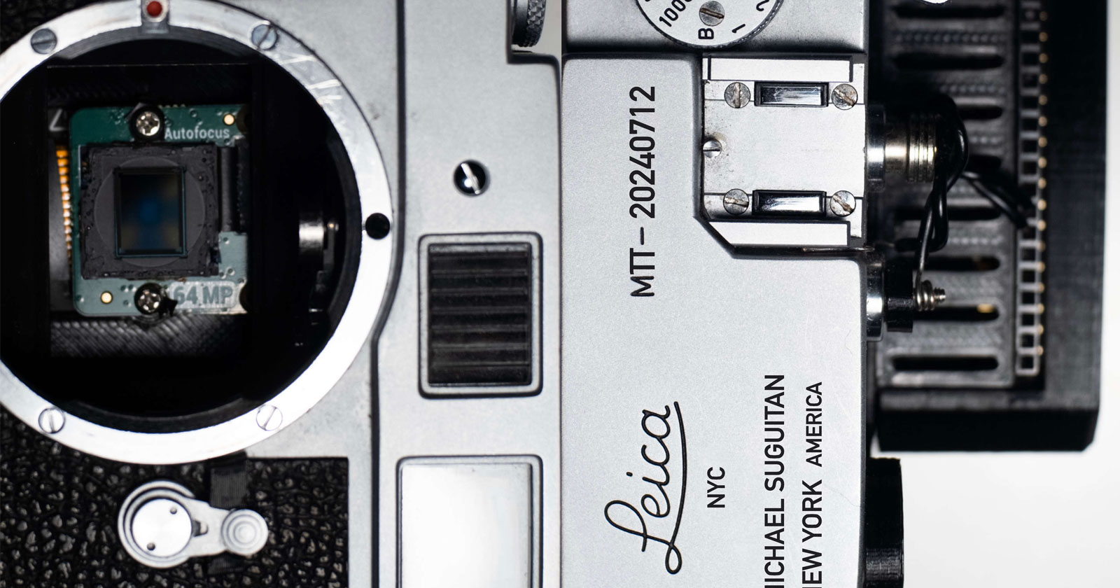 Close-up of a disassembled Leica camera showing its internal components, including the autofocus sensor and lens mount. Model number MT-20240712 is visible on the metal body, along with engravings Michael Suguitan and New York America.