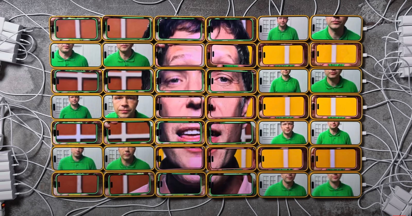 A collage of smartphone screens displays a man's face across multiple devices. Each screen shows a different part of the image, forming a complete face when viewed together. The phones are arranged in a grid, with chargers plugged in.