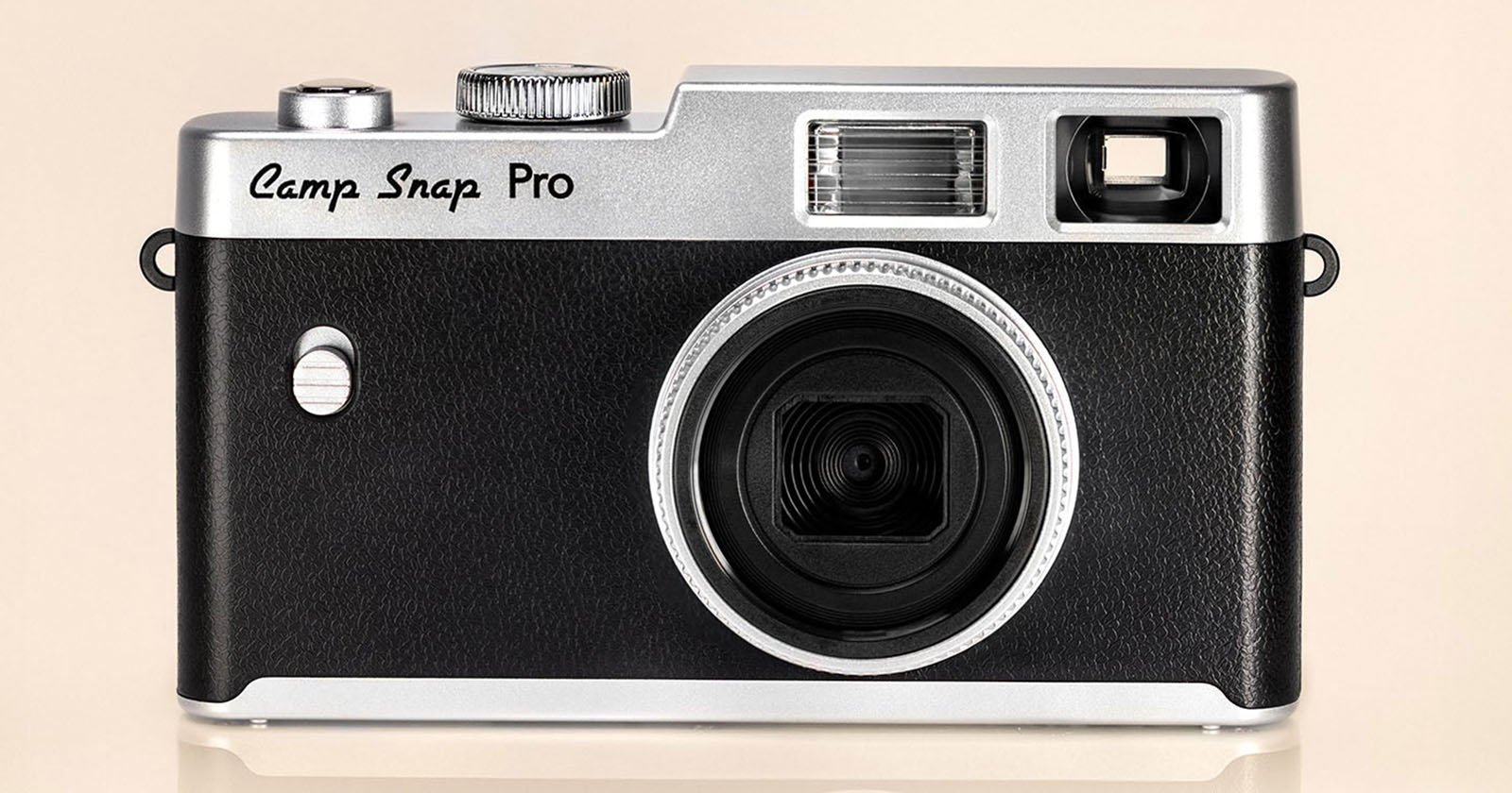 A black and silver retro-style digital camera labeled Camp Snap Pro, shown from the front against a beige background. The camera has a large lens, flash, and viewfinder.