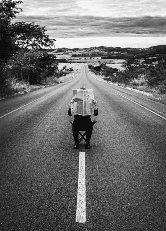 A man sitting in the middle of the street reading a newspaper