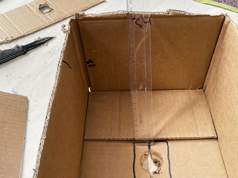 Using a ruler to measure the dimensions of a cardboard box to turn it into a DIY softbox