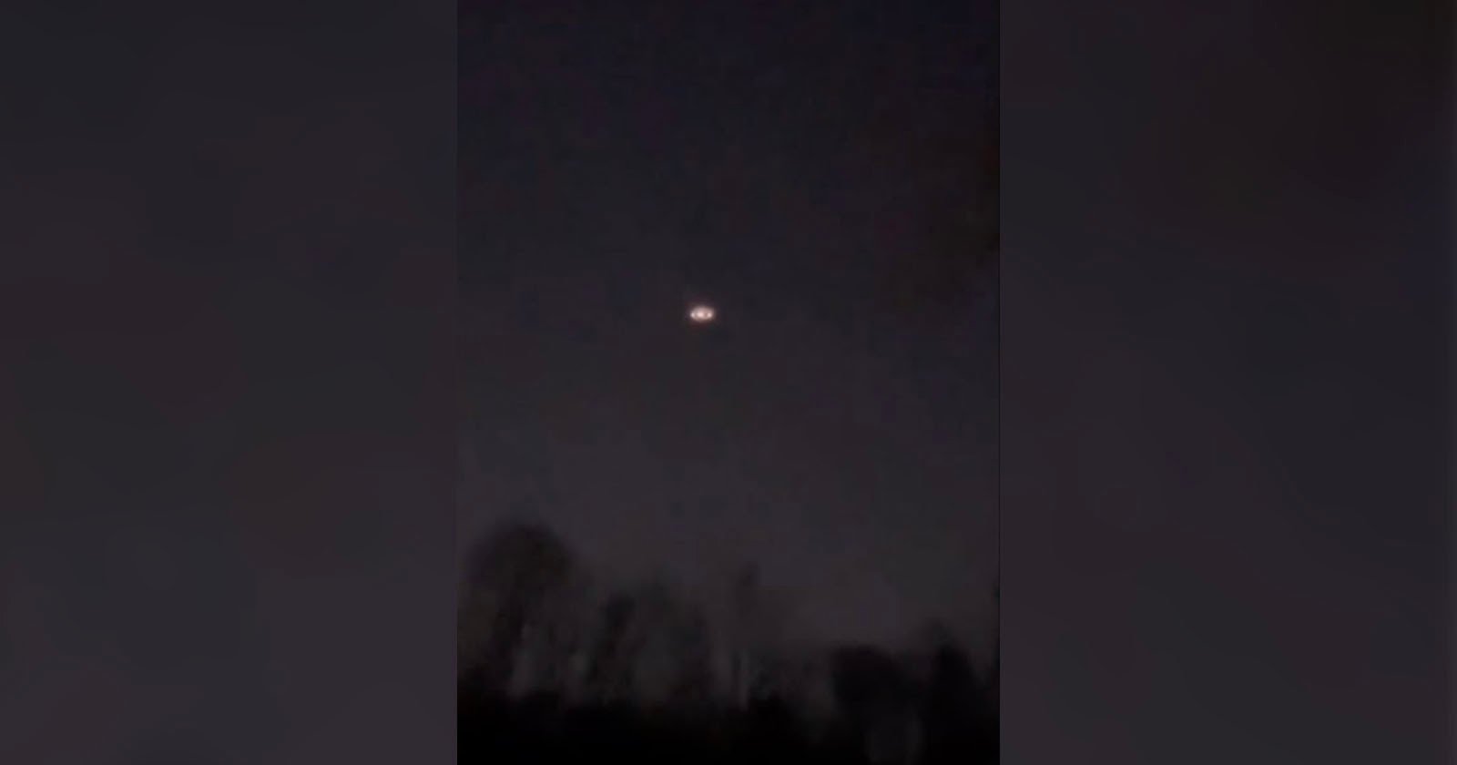 A dark sky with a faint, glowing object resembling a circular light is visible in the center. Silhouetted trees are at the bottom of the image, suggesting a nighttime scene.