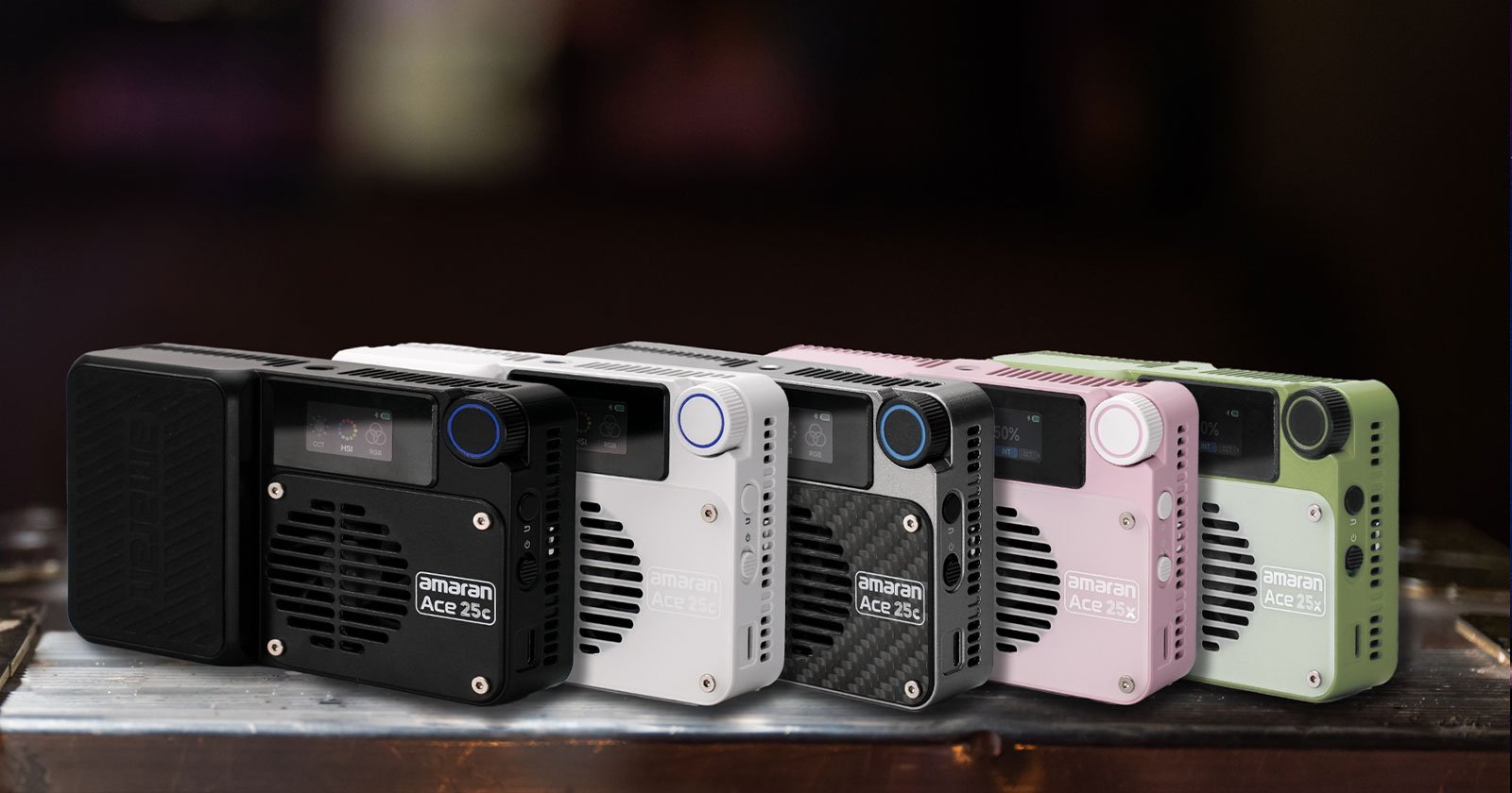 A row of five compact LED lights in various colors (black, white, gray, pink, and green) with a digital display and a vented design. They are placed on a reflective surface, showcasing their portable and modern design.