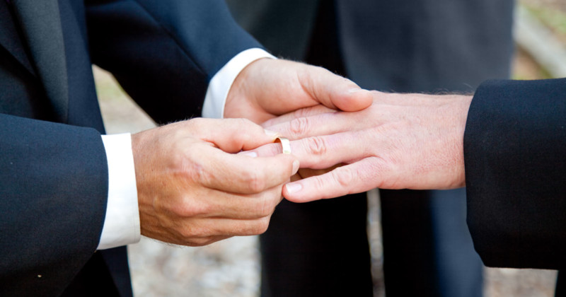 A man putting a wedding ring on another man at a wedding