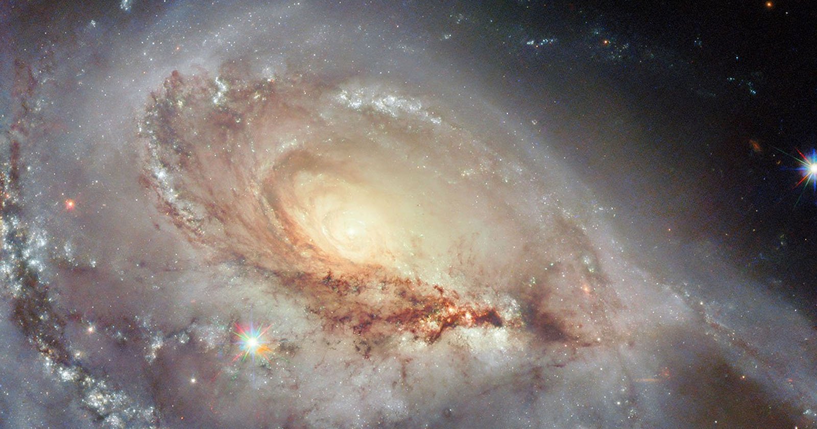 A stunning spiral galaxy with a bright, glowing center and swirling arms of stars, dust, and gas, set against a dark space background with distant star-like points of light.