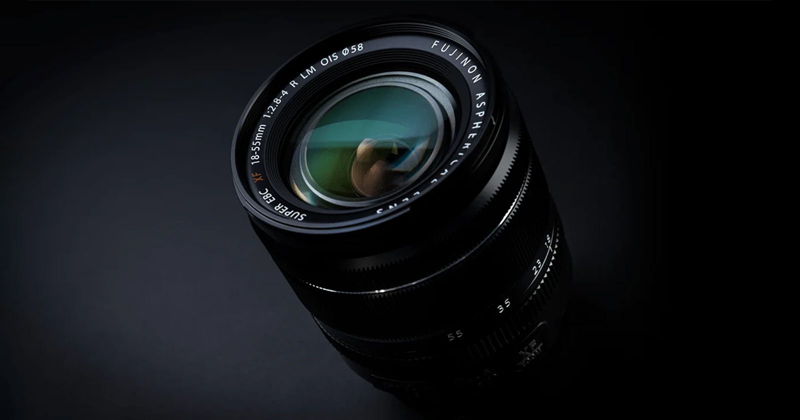 Close-up shot of a Fujinon camera lens against a black background. The lens has reflections visible on its glass, with the text Fujinon Aspherical Super EBC and the specifications 18-55mm 1:2.8-4 R LM OIS around the outer edge.