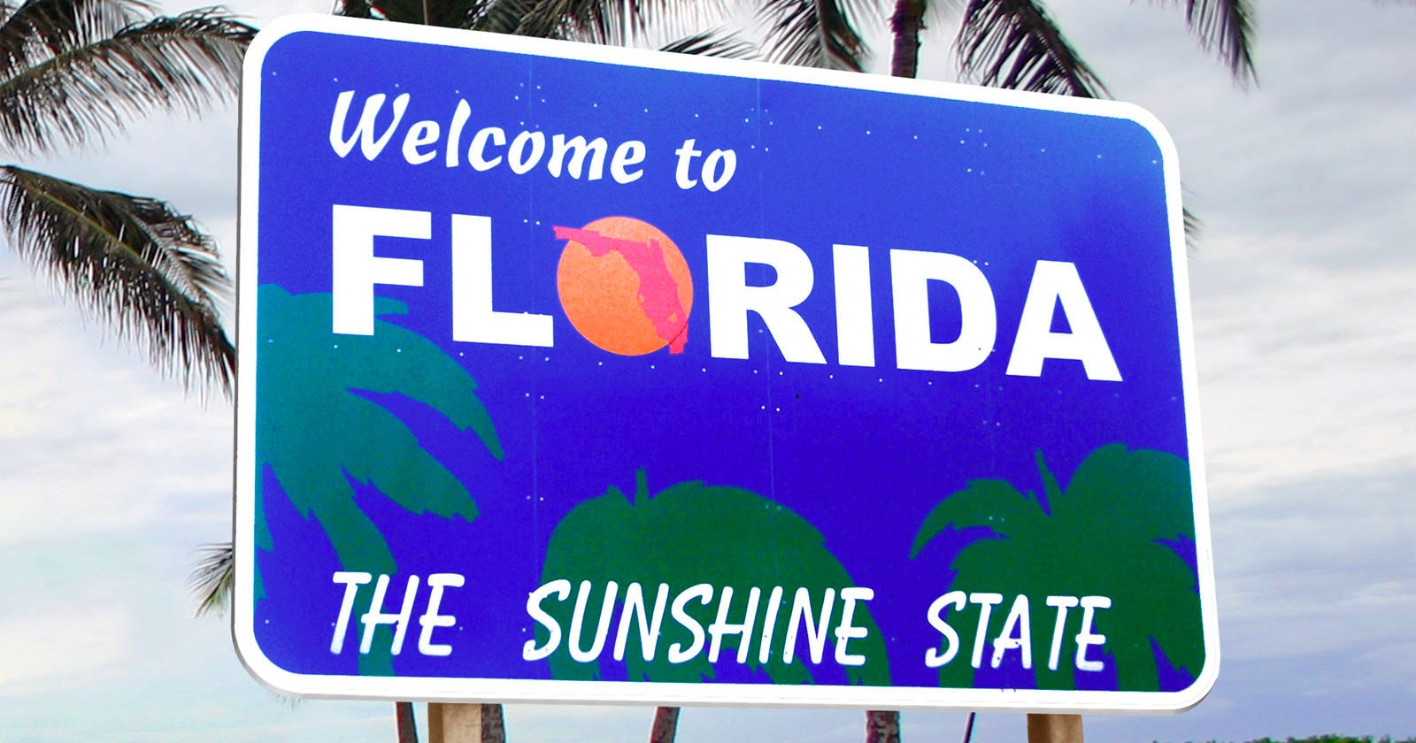 A road sign reads Welcome to Florida, The Sunshine State with a stylized orange in place of the o in Florida. Palm tree silhouettes are in the background, set against a cloudy sky.
