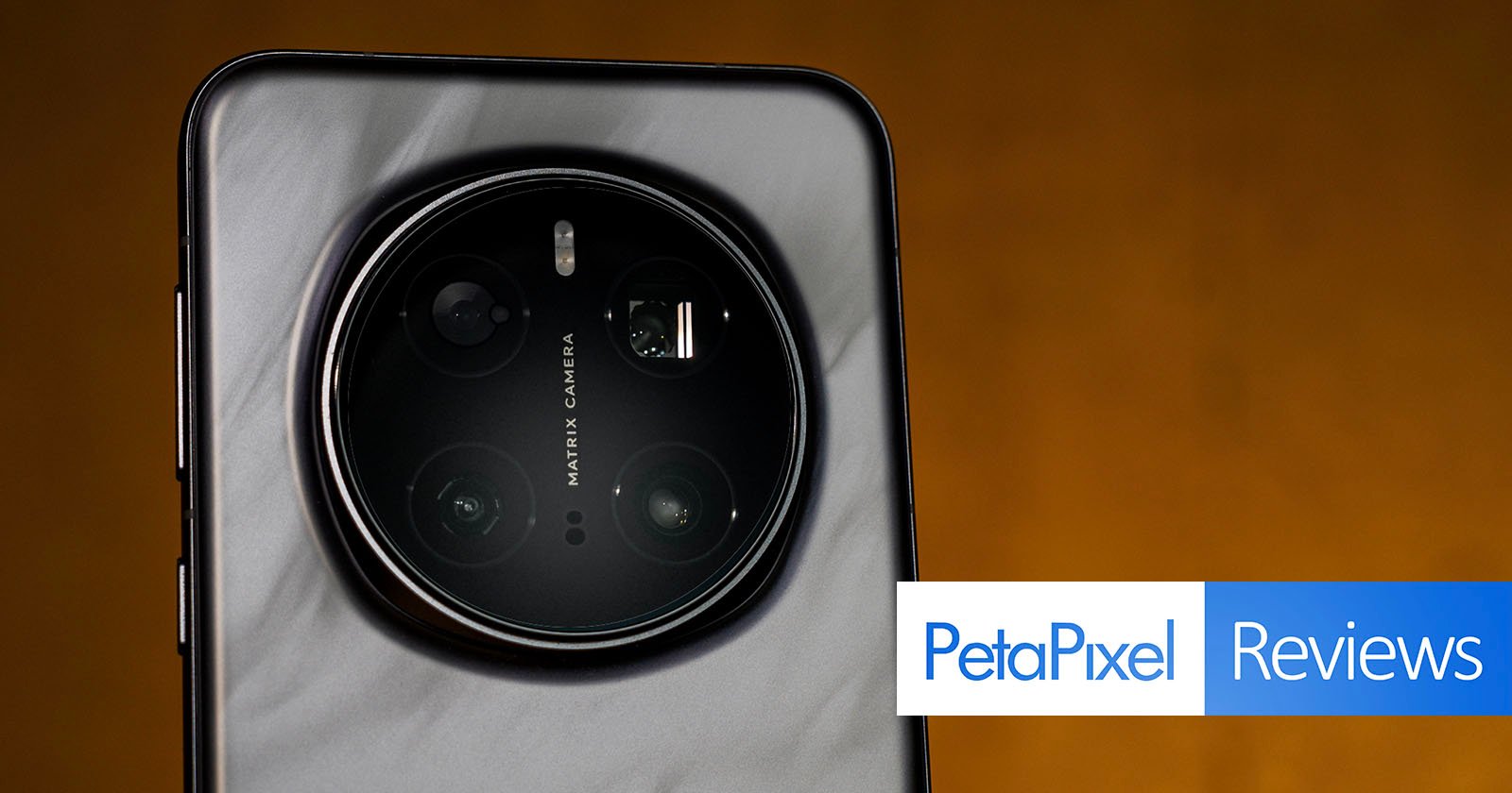 Close-up of a smartphone's rear camera setup, featuring a circular module with multiple lenses. The background is a warm brown tone. The Petapixel logo and the word Reviews appear at the bottom right.