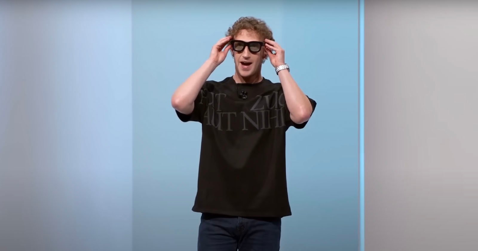 A person wearing a black shirt and glasses is standing and holding the glasses with both hands. The background is a gradient of light blue and white.