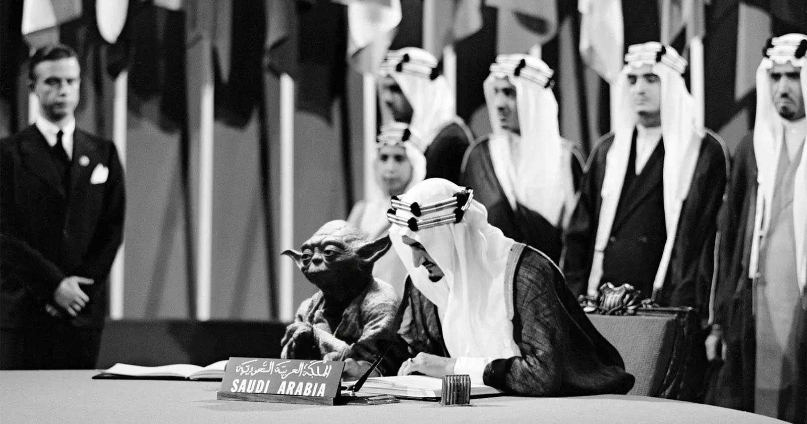 A black-and-white photo shows a person in traditional Saudi Arabian attire signing a document at a conference table labeled Saudi Arabia, with the Star Wars character Yoda seated beside him. Several men and international flags are in the background.