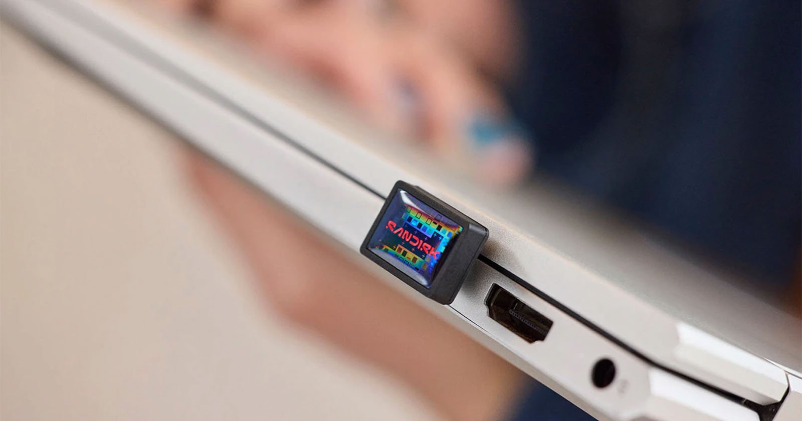 A close-up of a USB flash drive labeled REGULARS plugged into the side port of a silver laptop, with a blurred hand in the background.