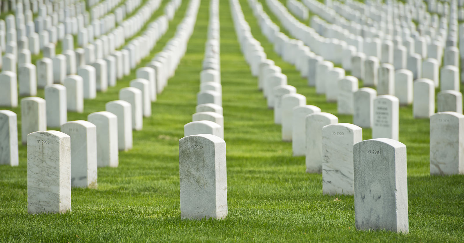 A solemn view of countless white headstones arranged in neat rows at a military cemetery, set on a well-manicured green lawn, reflecting the sacrifices of fallen soldiers. The headstones stretch into the distance, creating a poignant and respectful atmosphere.