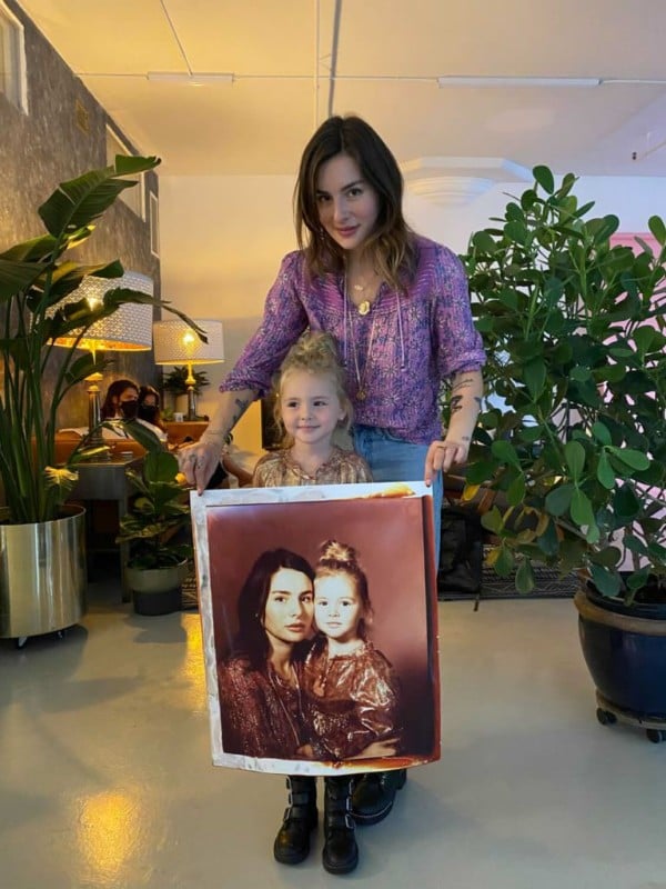 A woman and girl holding a large instant photo of themselves