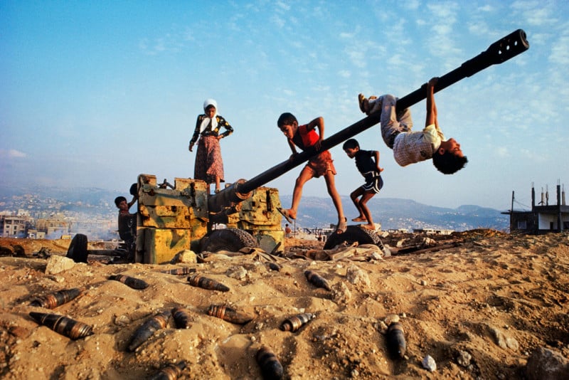 LEBANON-10001, Beirut, Lebanon, CAPTION: Children Play on Tank. Beirut, Lebanon, 1982. IG - 5.8.'17 Make-believe conquers the tools of war as children clamber over an abandoned anti-aircraft gun in Beirut, Lebanon, 1982. These tools of war became an improvised playground demonstrating the resilience of children. No matter how dire the situation, how dangerous the environment, children need to play. Whether it is splashing in puddles or climbing on abandoned tanks, their world of make believe is almost as important as food and shelter. MAX PRINT SIZE: 40x60 For children the detritus of war can function as an improvised playground. Derelict tanks, planes and military vehicles are often reclaimed as impromptu climbing frames. Yet, although the vehicle has been abandoned, an undercurrent of danger remains in the threat of numerous unexploded shells that litter the ground they play on. The irony of children playing on an abandoned tank, as if it were a 'jungle gym' in a schoolyard. In this photograph, the scene is heightened by the explosive potential of the shells at the children's feet. - Phaidon 55 National Geographic, February 1983, Beirut: Up From the Rubble Magnum Photos, NYC9206, MCS1982003K008. Phaidon, 55, Iconic Images, final book_iconic Make-believe conquers the tools of war as children clamber over an abandoned antiaircraft gun. Discarded shells around the gun may still be live, like the explosive grievances and vengeance harbored by many of Beirut's factions. Will there at least come a consensus that a time to bomb must give way to a time to rebuild? Ellis, William S. (February 1993_. Beirut -Up From the Rubble. National Geographic, Vol. 163, No. 2,284 Steve Mccurry_Book final print_MACRO final print_milan final print_Birmingham final print_HERMITAGE Graphic Novel_book Bonnie Book FINAL SELECT retouched_Sonny Fabbri, Sam Wallander 5/26/2018