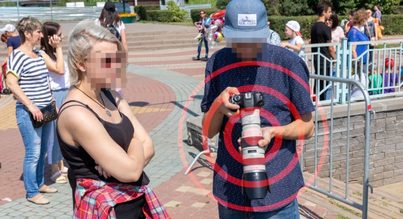 A man holding a Canon DSLR on a street with a red target on the camera