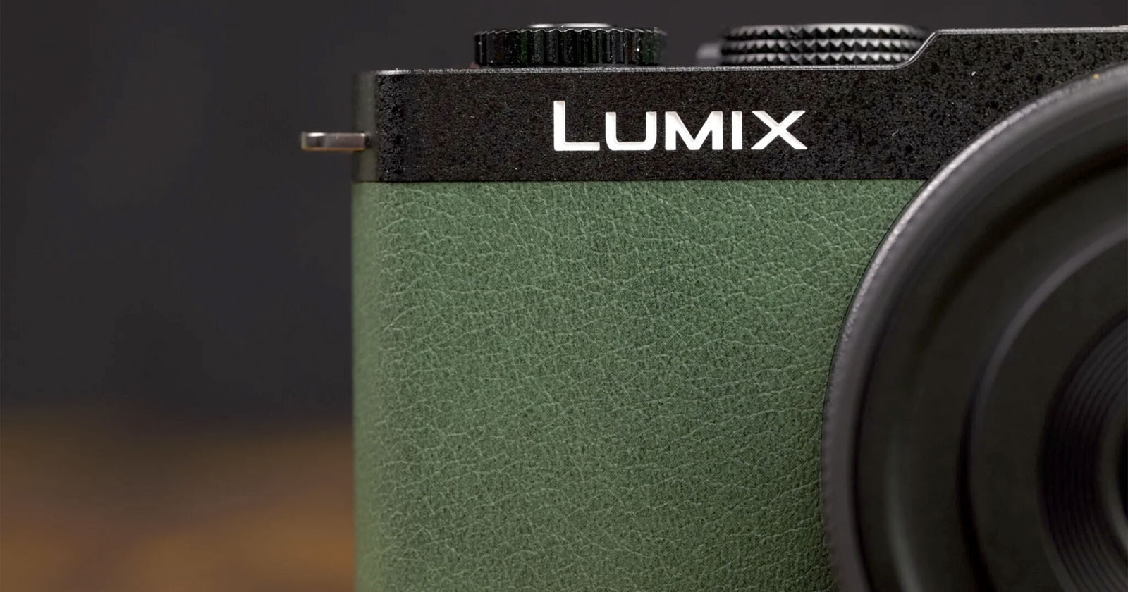 Close-up of a Lumix camera, showing the upper left portion. The camera features a black textured top with a black dial and a green textured grip. Part of the lens is visible on the right side of the image. The brand name Lumix is prominently displayed. Close-up of a Lumix camera, showing the upper left portion. The camera features a black textured top with a black dial and a green textured grip. Part of the lens is visible on the right side of the image. The brand name Lumix is prominently displayed.