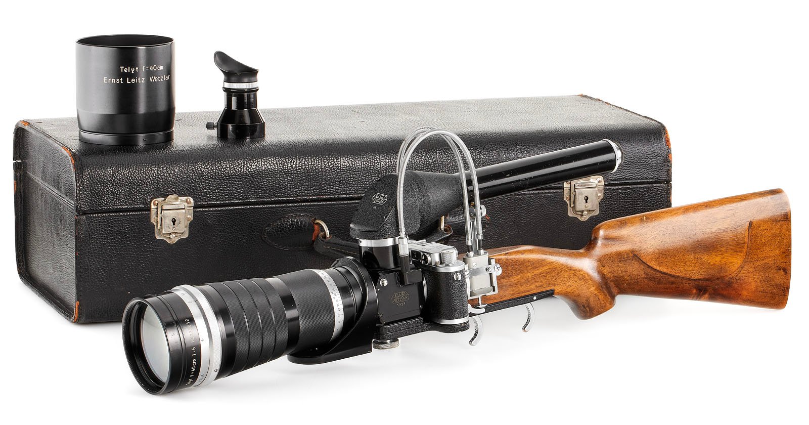 Vintage camera with a telephoto lens attached to a rifle stock for stabilization, alongside additional lenses and a carrying case. Vintage camera with a telephoto lens attached to a rifle stock for stabilization, alongside additional lenses and a carrying case.