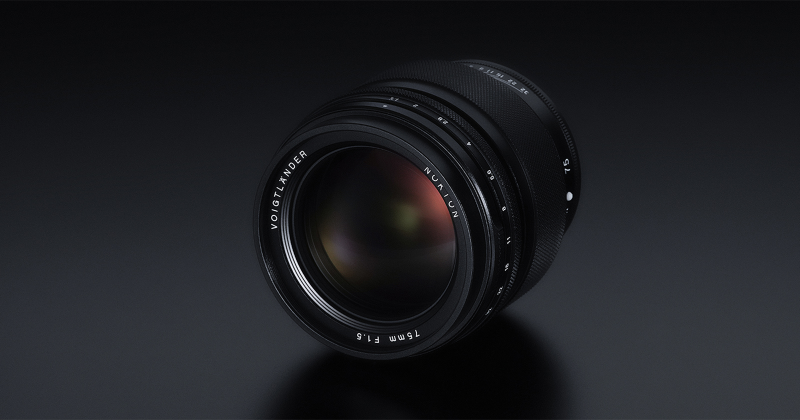A close-up view of a Voigtländer Nokton 75mm f/1.5 lens resting on a dark surface. The lens features a sleek black design with white text around the front element indicating the brand, model, and aperture specifications. A close-up view of a Voigtländer Nokton 75mm f/1.5 lens resting on a dark surface. The lens features a sleek black design with white text around the front element indicating the brand, model, and aperture specifications.