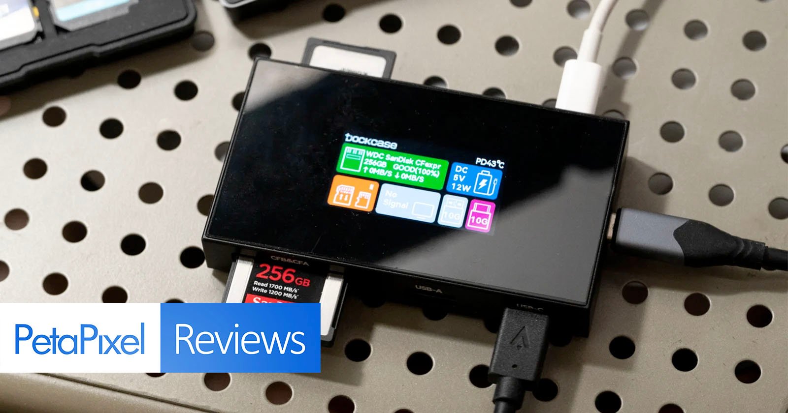 A close-up of a black device with a screen displaying various power-related information, including Bookcase and different voltage and current readings. Several cables and a 256GB SD card are connected to the device. The image includes a PetaPixel Reviews label. A close-up of a black device with a screen displaying various power-related information, including Bookcase and different voltage and current readings. Several cables and a 256GB SD card are connected to the device. The image includes a PetaPixel Reviews label.