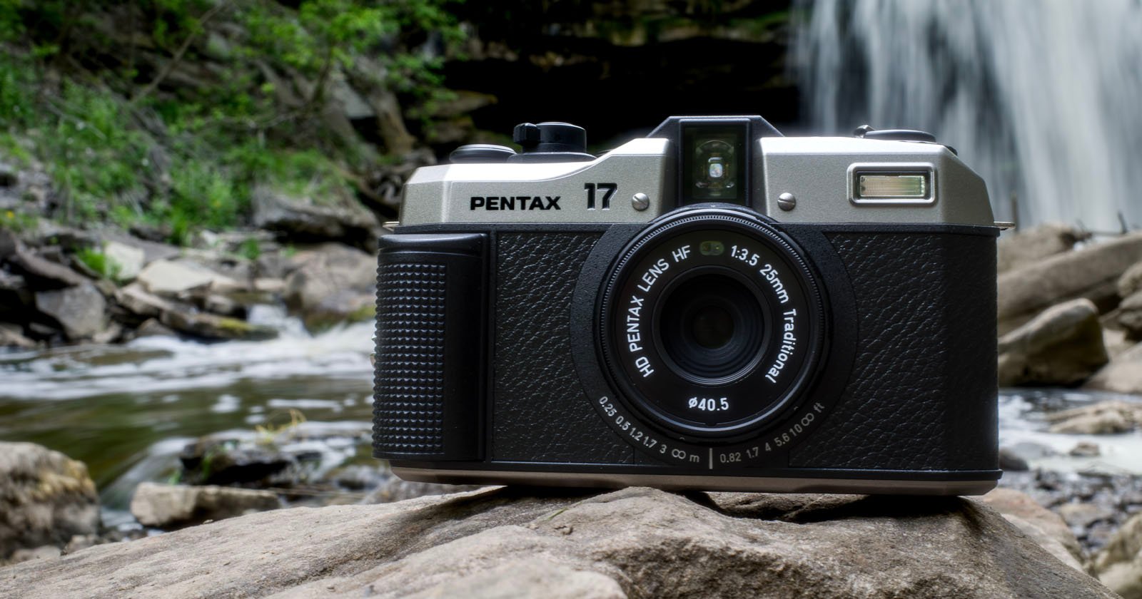 A vintage Pentax 17 camera sits on a rock with a waterfall and lush greenery in the background. The camera is positioned slightly to the right, highlighting its lens and intricate design amidst the natural setting. A vintage Pentax 17 camera sits on a rock with a waterfall and lush greenery in the background. The camera is positioned slightly to the right, highlighting its lens and intricate design amidst the natural setting.