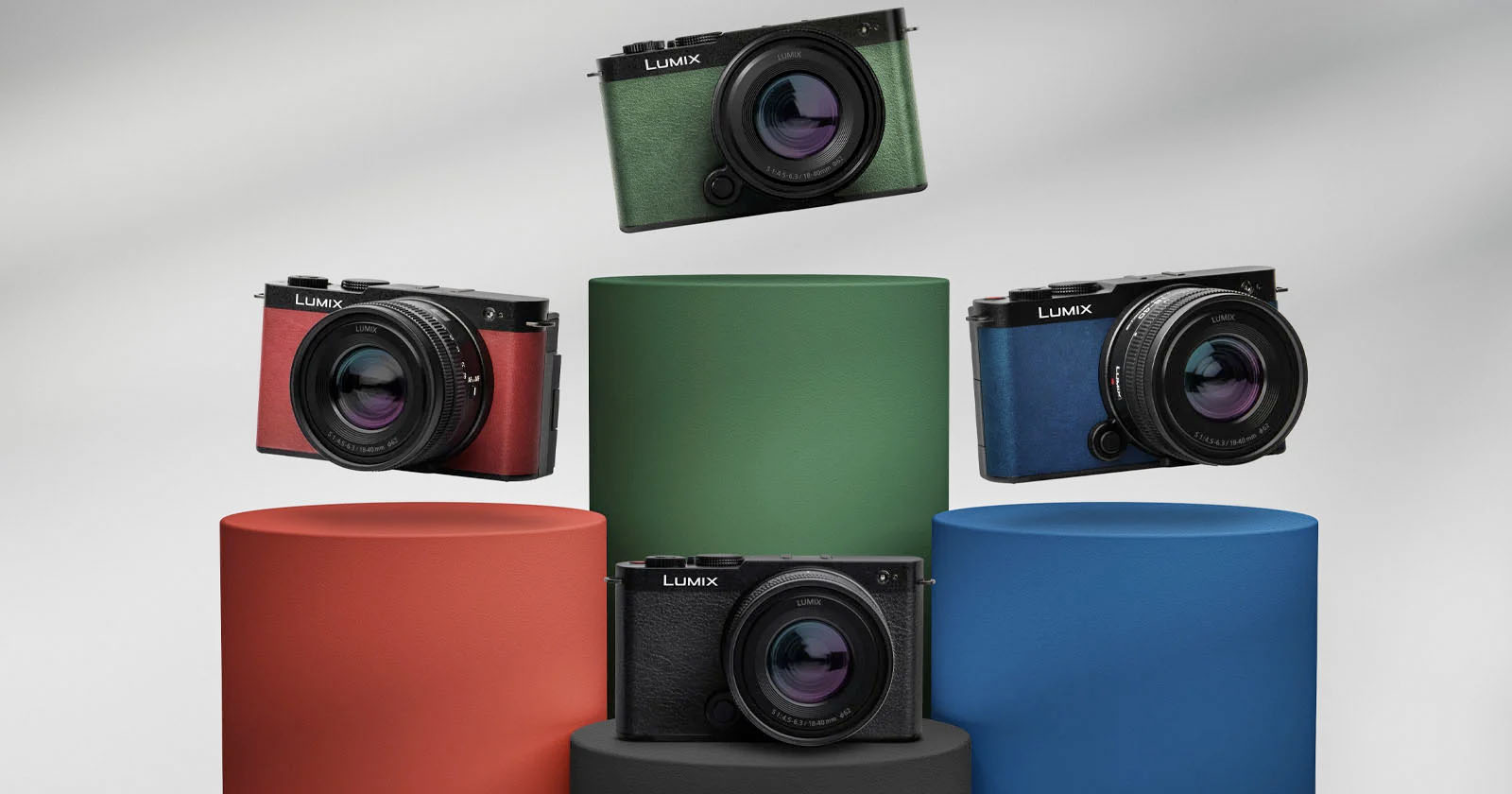 Four Lumix cameras with different body colors (red, green, blue, and black) are displayed on colorful cylindrical pedestals (orange, green, blue, and black) against a neutral background. Each camera has a large lens, and the arrangement showcases the variety available. Four Lumix cameras with different body colors (red, green, blue, and black) are displayed on colorful cylindrical pedestals (orange, green, blue, and black) against a neutral background. Each camera has a large lens, and the arrangement showcases the variety available.