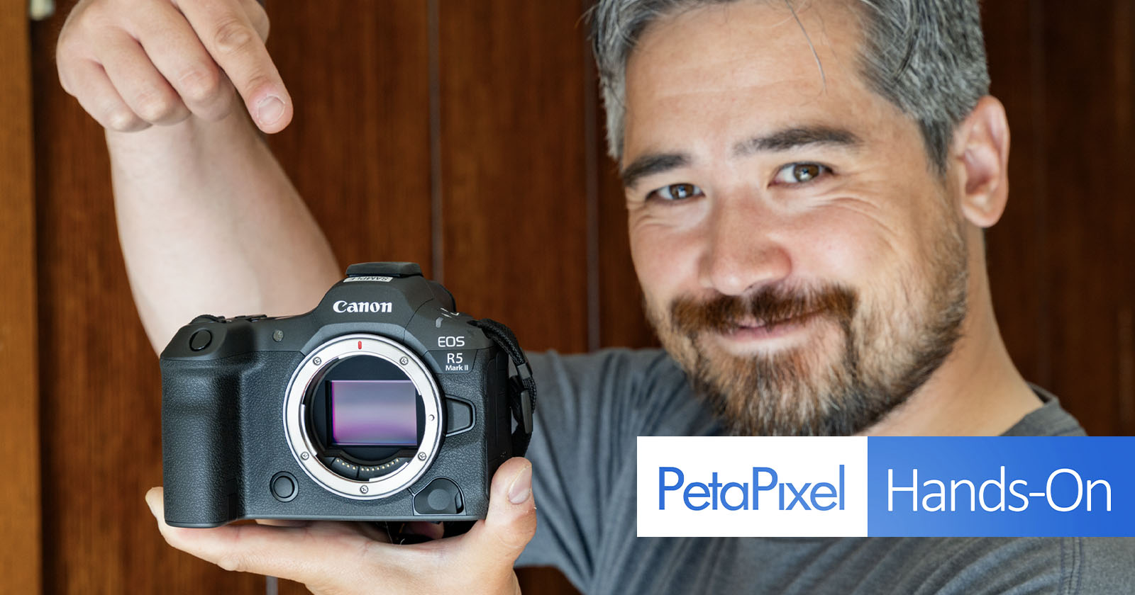 A person with gray hair and a beard smiles and points to a Canon EOS R5 camera with the lens removed, showcasing the camera sensor. The image has a PetaPixel Hands-On logo in the bottom left corner. A person with gray hair and a beard smiles and points to a Canon EOS R5 camera with the lens removed, showcasing the camera sensor. The image has a PetaPixel Hands-On logo in the bottom left corner.