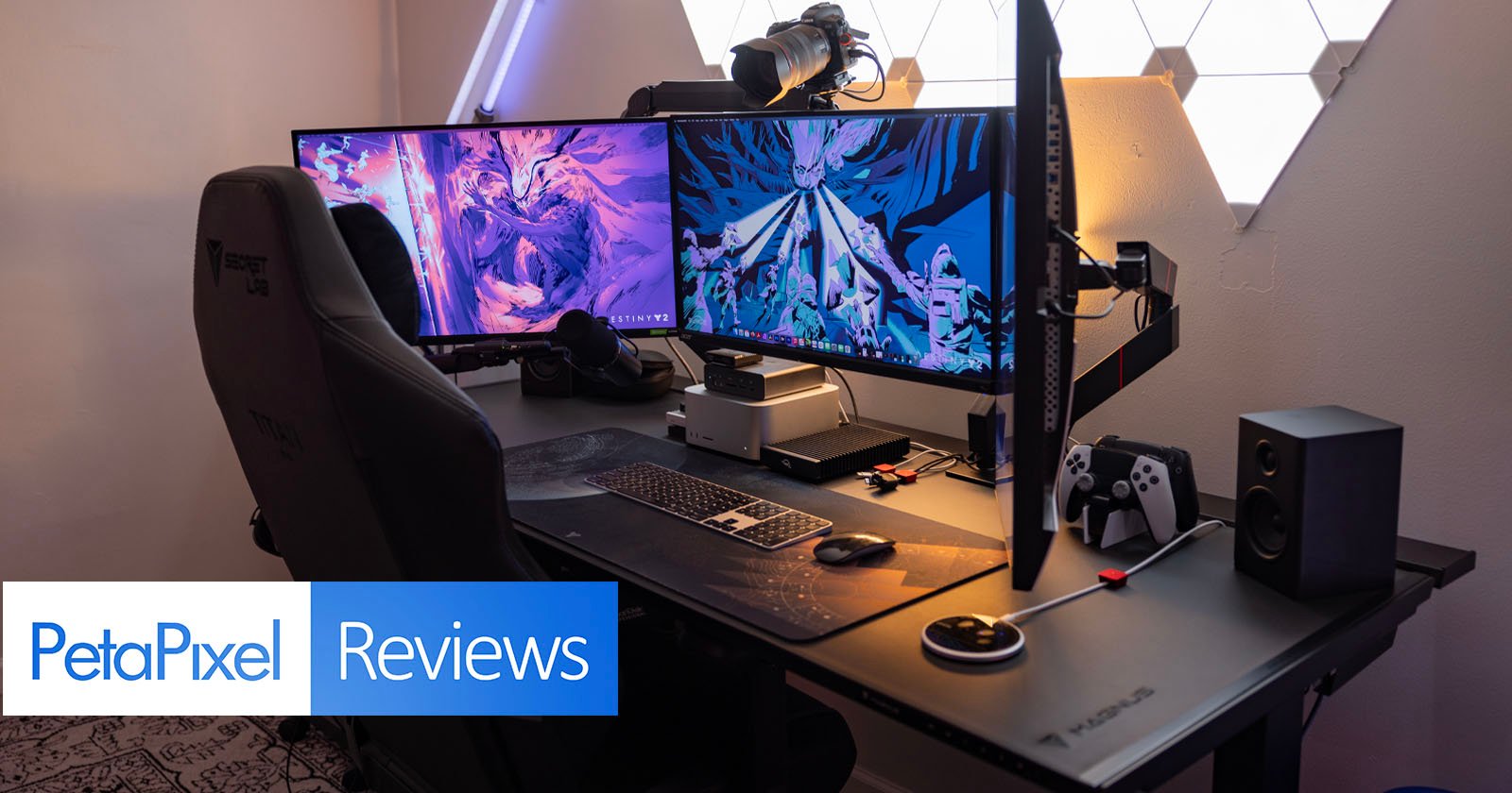 A modern gaming desk setup with dual monitors displaying vibrant, colorful graphics. The desk includes gaming peripherals like a mouse, keyboard, controller, headphones, and speakers. A PetaPixel Reviews label is visible in the foreground. A modern gaming desk setup with dual monitors displaying vibrant, colorful graphics. The desk includes gaming peripherals like a mouse, keyboard, controller, headphones, and speakers. A PetaPixel Reviews label is visible in the foreground.