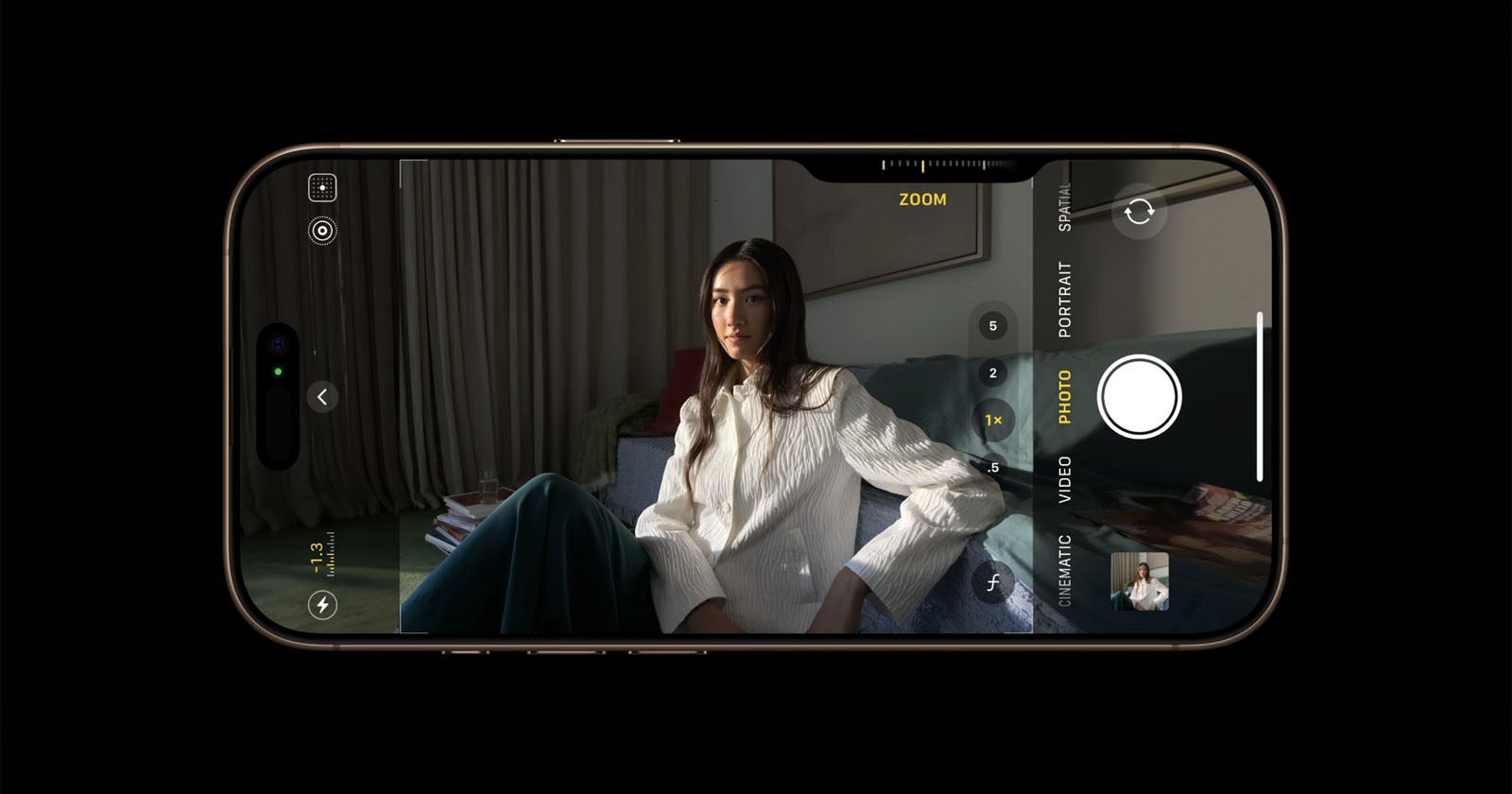A smartphone display shows a camera app interface capturing a woman who is sitting on a couch with her arms crossed. The woman has long hair and is dressed in a white top and green pants. Various camera settings are visible on the screen. A smartphone display shows a camera app interface capturing a woman who is sitting on a couch with her arms crossed. The woman has long hair and is dressed in a white top and green pants. Various camera settings are visible on the screen.