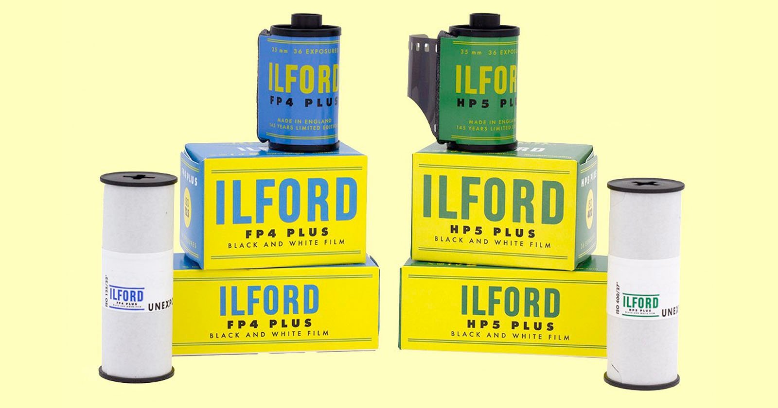 The image shows several boxes and rolls of ILFORD black and white film. The boxes are labeled HP5 Plus and FP4 Plus and are yellow with blue and black text. Four film canisters are positioned around the boxes, two of which are in gray film canisters. The image shows several boxes and rolls of ILFORD black and white film. The boxes are labeled HP5 Plus and FP4 Plus and are yellow with blue and black text. Four film canisters are positioned around the boxes, two of which are in gray film canisters.