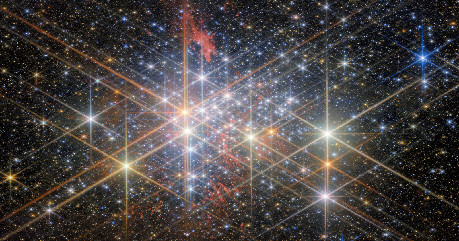 A vibrant star cluster set against a dark space background. Numerous stars shine brightly, with diffraction spikes creating starburst effects. Wisps of red nebula gas are interspersed throughout, adding texture and depth to the celestial scene. A vibrant star cluster set against a dark space background. Numerous stars shine brightly, with diffraction spikes creating starburst effects. Wisps of red nebula gas are interspersed throughout, adding texture and depth to the celestial scene.