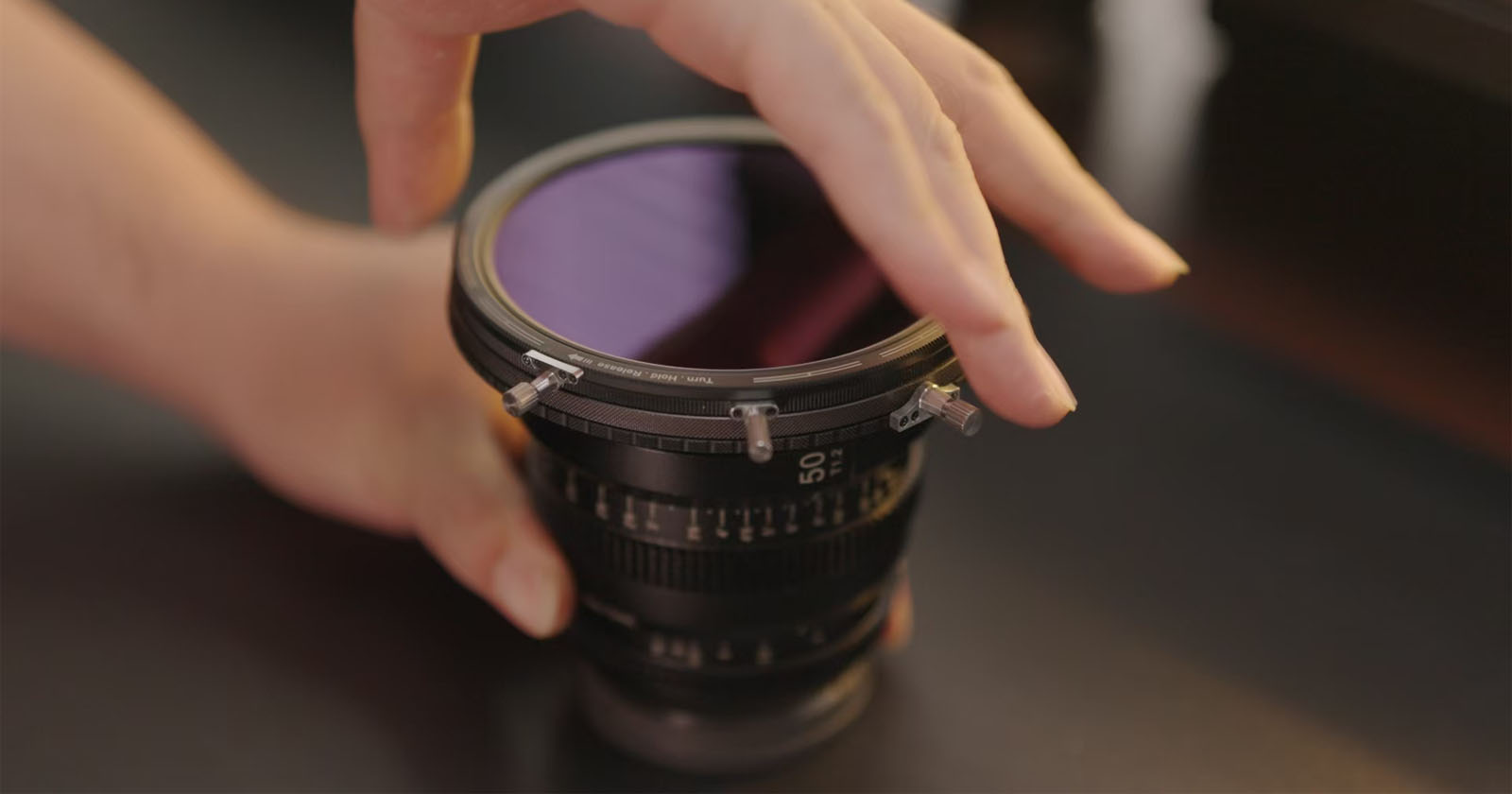 A person adjusts a circular filter on a camera lens. The scene captures a close-up of the hands gently handling the filter on a 50mm lens, with a blurred background. A person adjusts a circular filter on a camera lens. The scene captures a close-up of the hands gently handling the filter on a 50mm lens, with a blurred background.