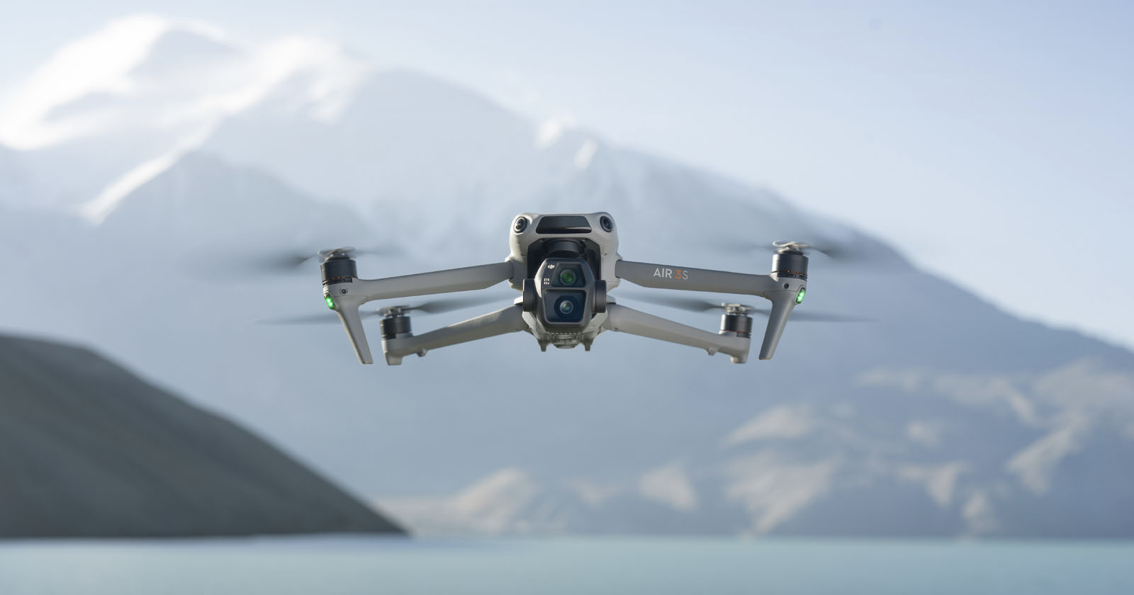 A drone hovers in the foreground against a backdrop of snow-capped mountains and a calm lake. The sky is clear and blue. A drone hovers in the foreground against a backdrop of snow-capped mountains and a calm lake. The sky is clear and blue.