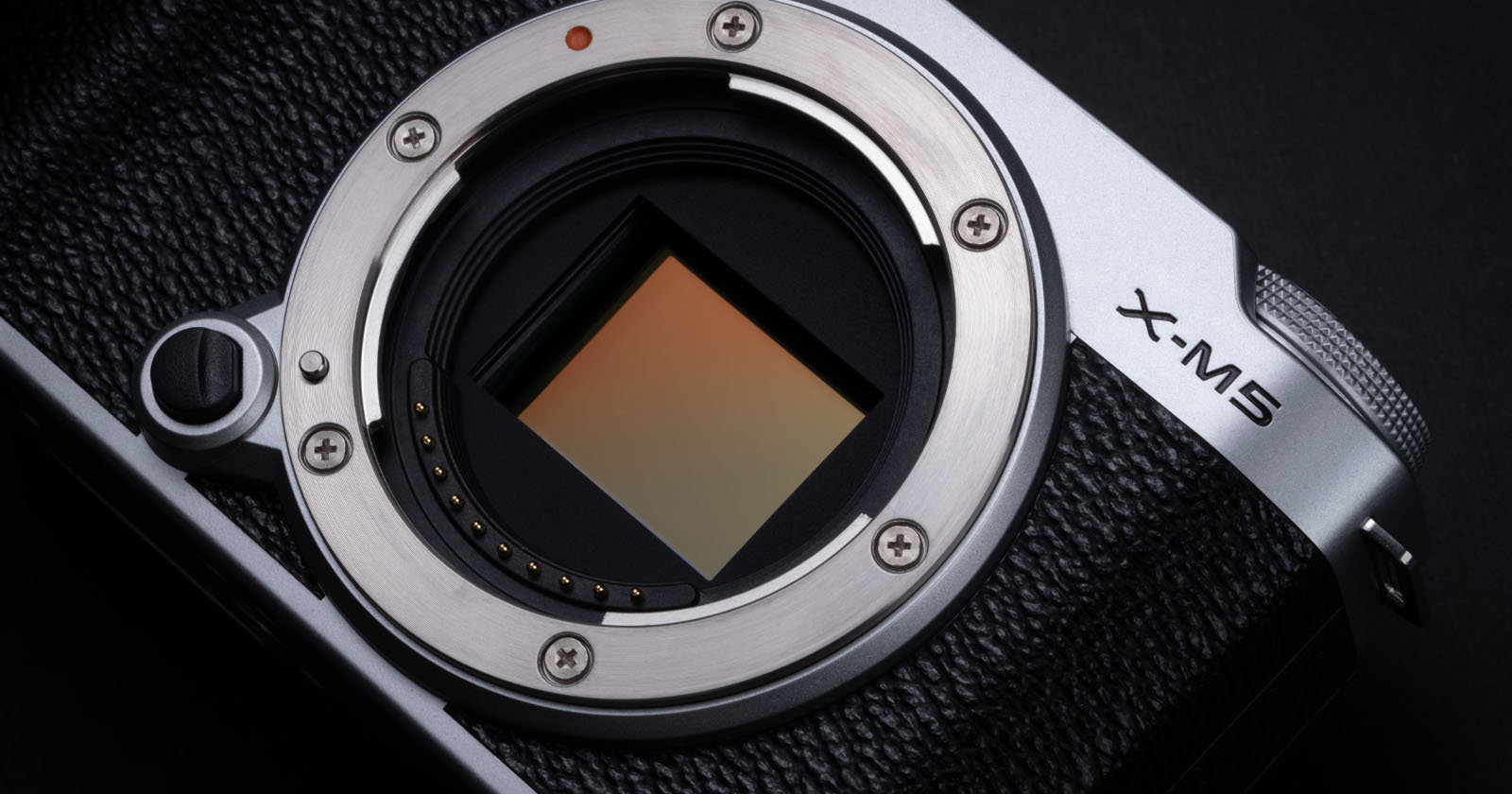 Close-up of a silver and black camera body without a lens, showing the sensor inside the metal mount. The model is labeled X-M5 on the top right corner, with textured black grip on the left side. Close-up of a silver and black camera body without a lens, showing the sensor inside the metal mount. The model is labeled X-M5 on the top right corner, with textured black grip on the left side.