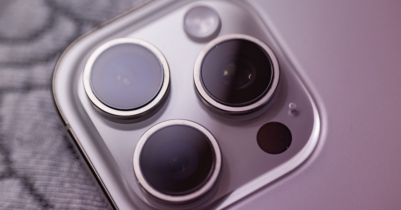 Close-up of a smartphone's rear camera system featuring three lenses and a flash, set against a blurred gray background. The lenses are arranged in a triangular pattern. Close-up of a smartphone's rear camera system featuring three lenses and a flash, set against a blurred gray background. The lenses are arranged in a triangular pattern.
