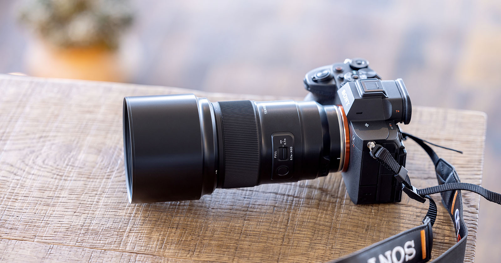 A black camera with a large telephoto lens rests on a wooden table. The camera strap, partially visible, is branded with SONY. The background is softly blurred, highlighting the camera as the focal point. A black camera with a large telephoto lens rests on a wooden table. The camera strap, partially visible, is branded with SONY. The background is softly blurred, highlighting the camera as the focal point.
