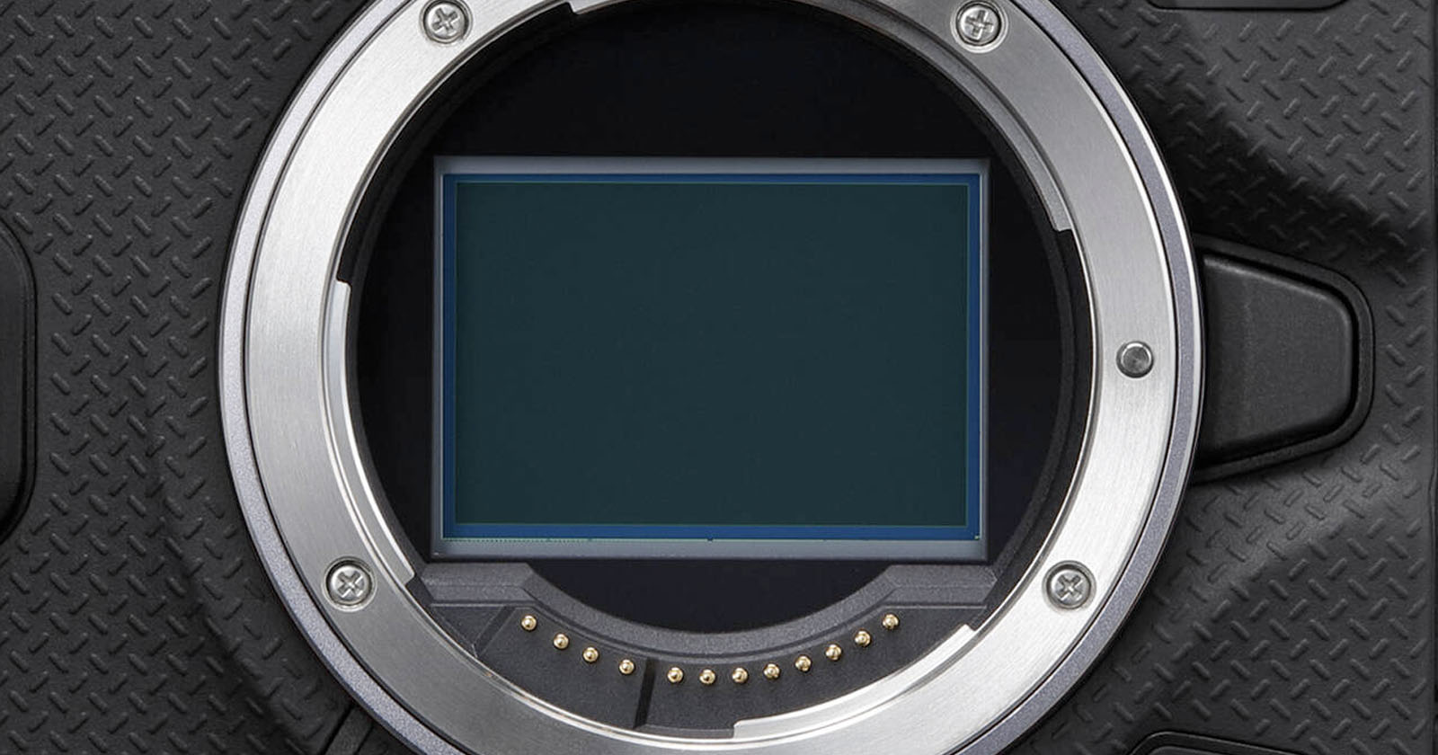 Close-up of a digital camera's sensor, surrounded by a metal mount. The camera's body has a textured black surface. The sensor is rectangular, with electronic contacts visible along the mount's inner edge. Close-up of a digital camera's sensor, surrounded by a metal mount. The camera's body has a textured black surface. The sensor is rectangular, with electronic contacts visible along the mount's inner edge.