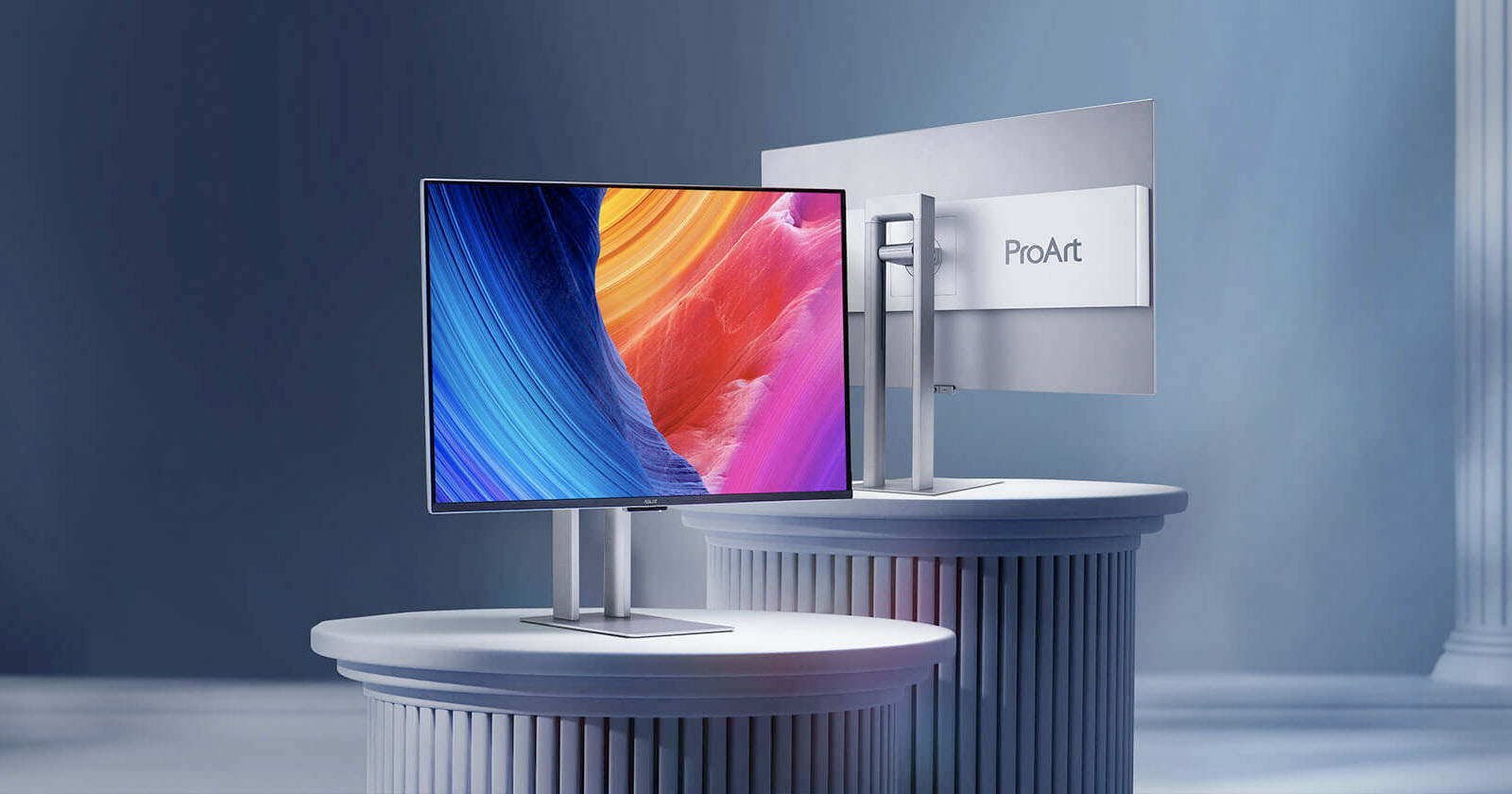 A sleek computer monitor with vibrant abstract colors on the screen is displayed from both front and rear views. The monitor is mounted on a silver stand and labeled ProArt. Both are positioned on elegant cylindrical pedestals. A sleek computer monitor with vibrant abstract colors on the screen is displayed from both front and rear views. The monitor is mounted on a silver stand and labeled ProArt. Both are positioned on elegant cylindrical pedestals.