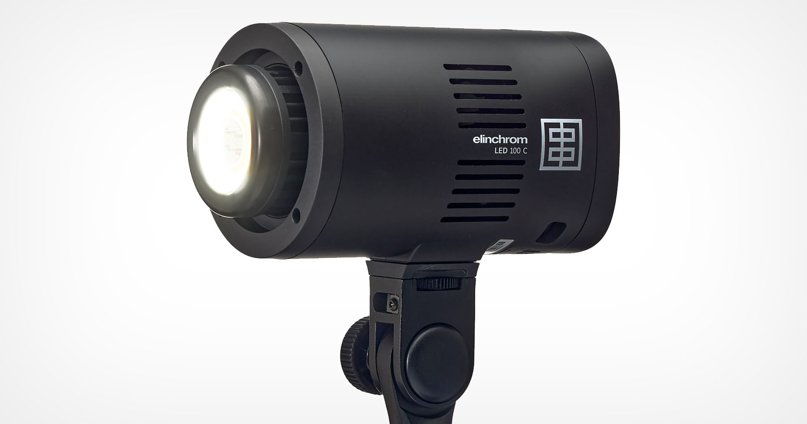 A black Elinchrom LED 100 D light mounted on a stand. The light is turned on, emitting a bright glow. The body has vents for cooling and displays the brand name and model. A black Elinchrom LED 100 D light mounted on a stand. The light is turned on, emitting a bright glow. The body has vents for cooling and displays the brand name and model.