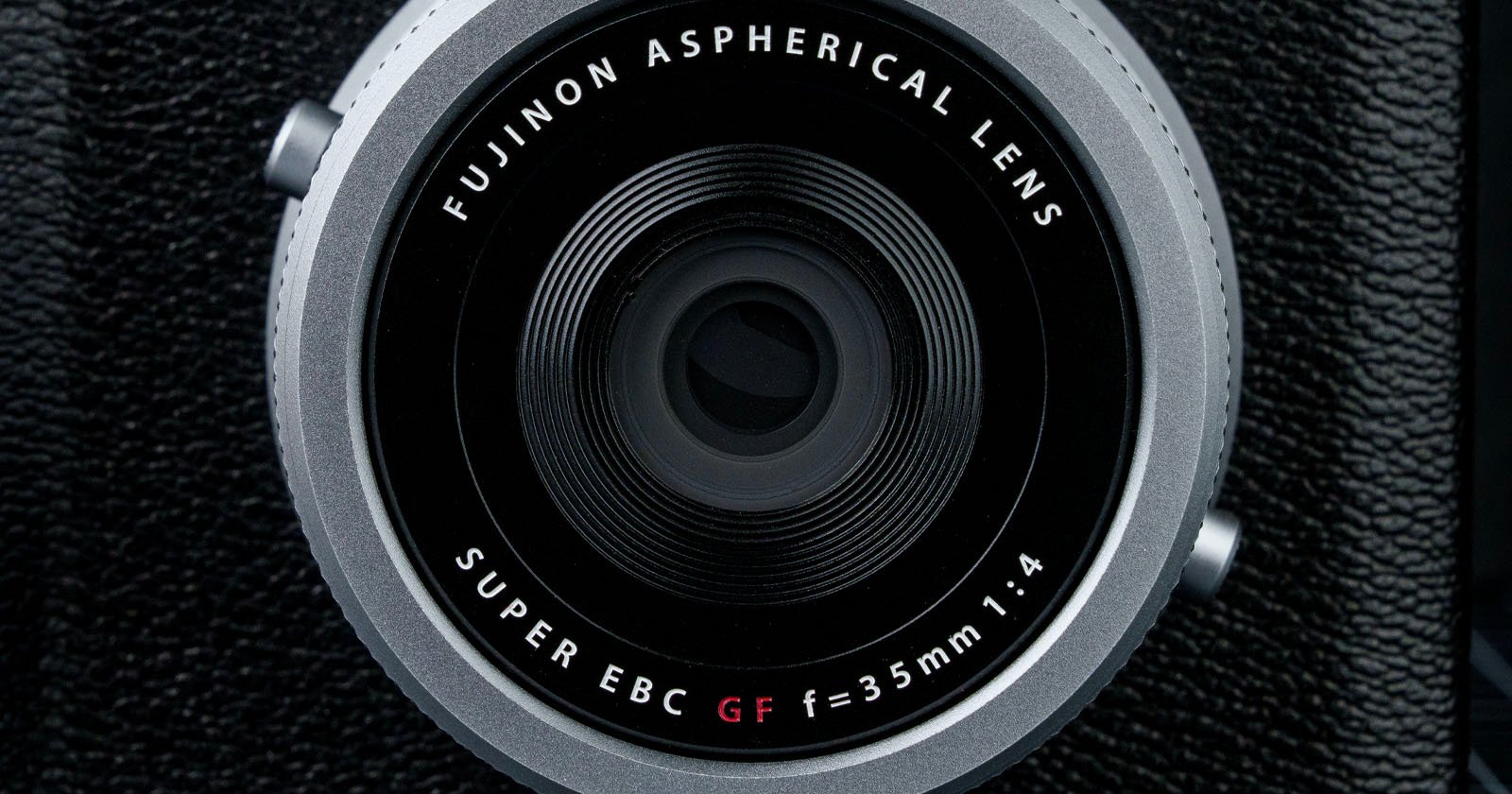 Close-up of a Fujinon Aspherical Lens. The text on the lens reads FUJINON ASPHERICAL LENS, SUPER EBC GF f=35mm 1:4. The lens is surrounded by a textured black surface. Close-up of a Fujinon Aspherical Lens. The text on the lens reads FUJINON ASPHERICAL LENS, SUPER EBC GF f=35mm 1:4. The lens is surrounded by a textured black surface.