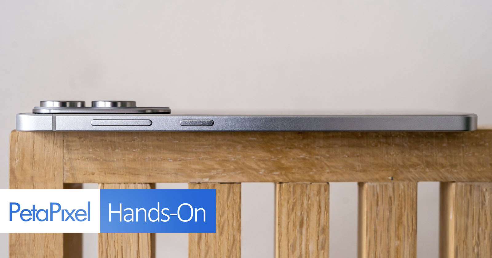 A side view of a silver smartphone with prominent camera bumps, resting on a wooden surface. The image features the PetaPixel Hands-On logo in the bottom left corner. A side view of a silver smartphone with prominent camera bumps, resting on a wooden surface. The image features the PetaPixel Hands-On logo in the bottom left corner.