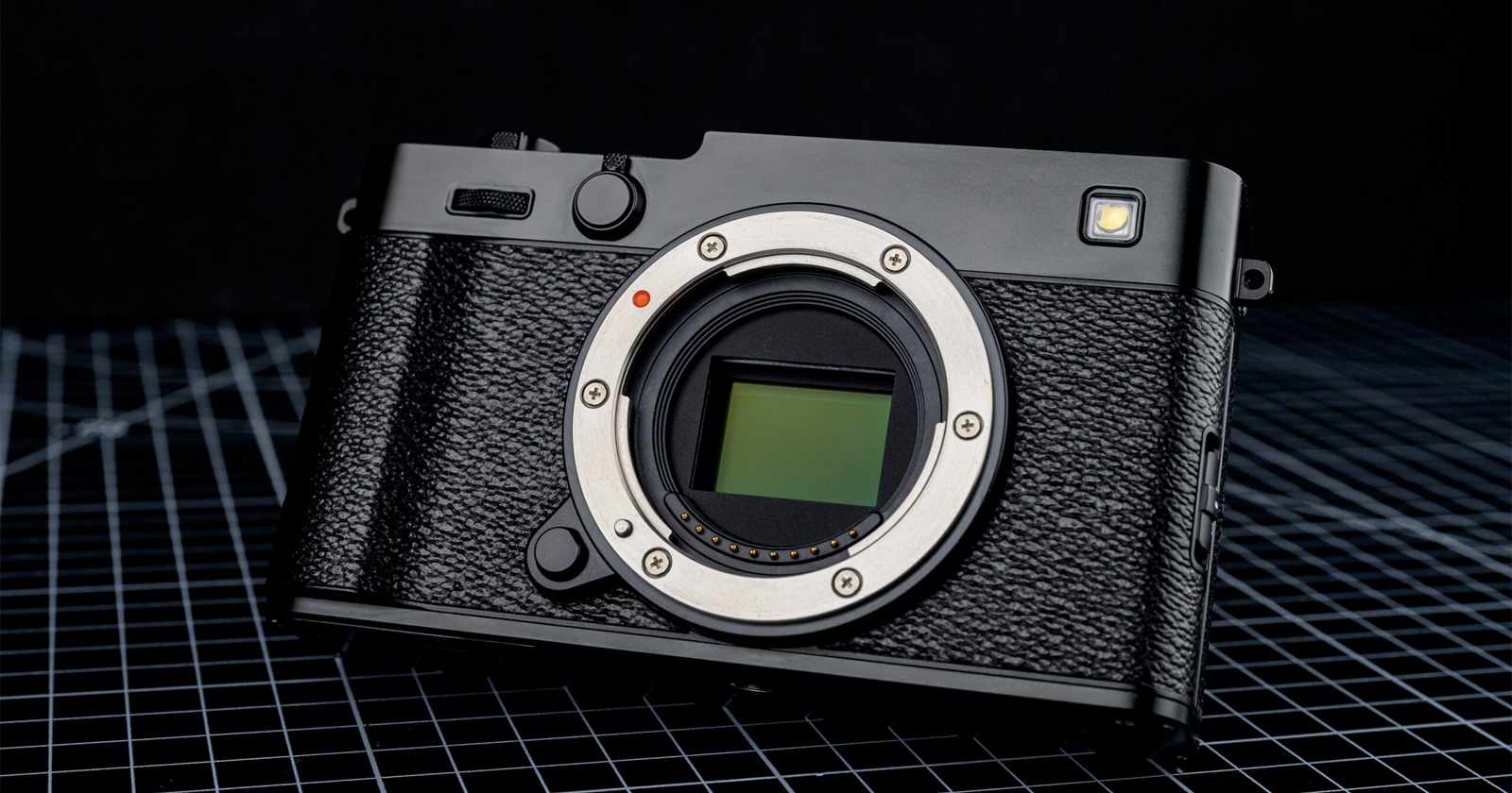 A black digital camera body without a lens is displayed on a grid-patterned surface, showing its sensor and textured grip, with a dark background behind it. A black digital camera body without a lens is displayed on a grid-patterned surface, showing its sensor and textured grip, with a dark background behind it.