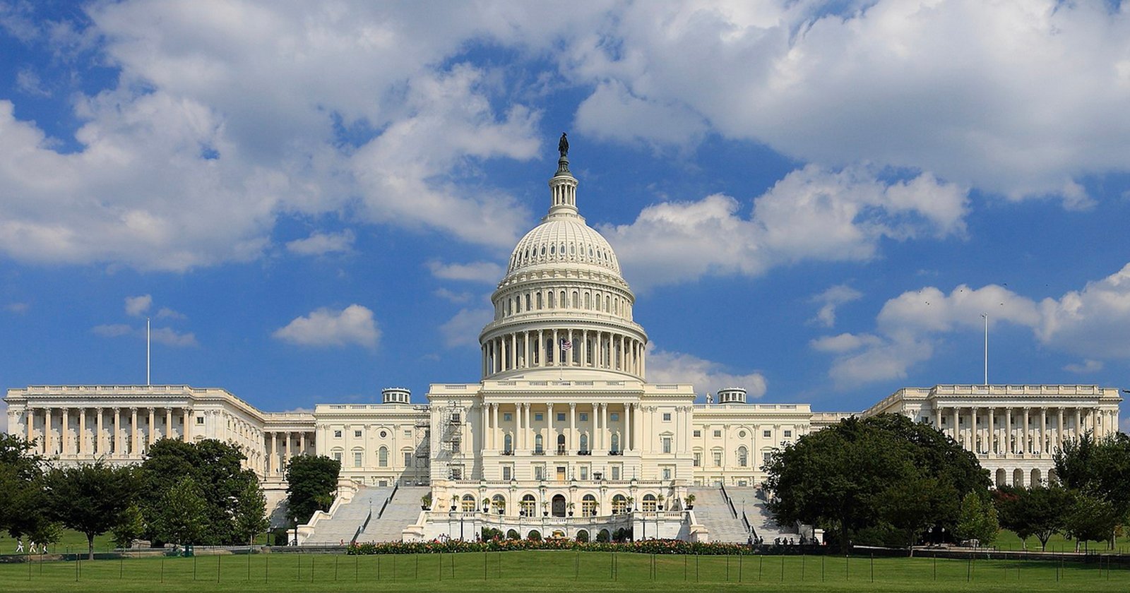 The United States Capitol building with its white dome and columns, set against a blue sky with scattered clouds and surrounded by green lawns and trees. The United States Capitol building with its white dome and columns, set against a blue sky with scattered clouds and surrounded by green lawns and trees.