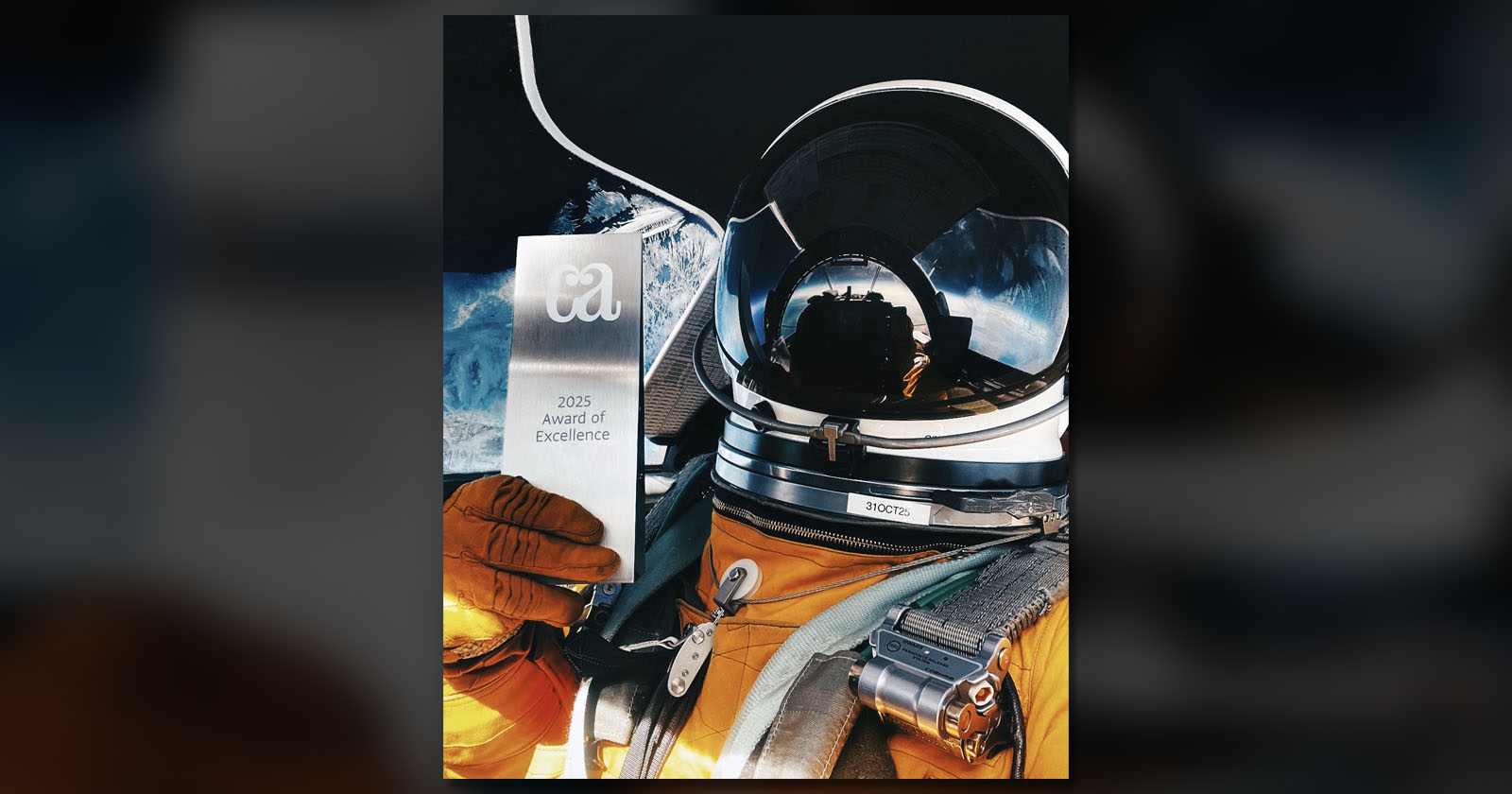 An astronaut in an orange suit holds a trophy labeled ca 2025 Award of Excellence, with a blue sky and clouds reflected in the helmet's visor. An astronaut in an orange suit holds a trophy labeled ca 2025 Award of Excellence, with a blue sky and clouds reflected in the helmet's visor.