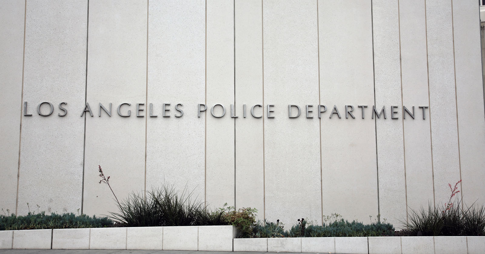 Large, modern concrete building facade with Los Angeles Police Department in metal letters; low landscaping with various small plants in front. Large, modern concrete building facade with Los Angeles Police Department in metal letters; low landscaping with various small plants in front.
