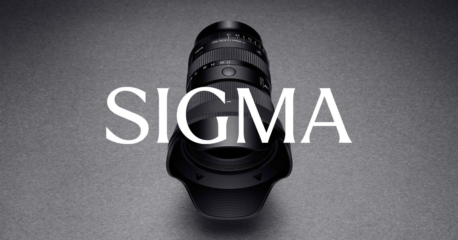 A Sigma camera lens with a lens hood is positioned vertically on a gray surface, with the word SIGMA in large white letters overlaid across the image. A Sigma camera lens with a lens hood is positioned vertically on a gray surface, with the word SIGMA in large white letters overlaid across the image.