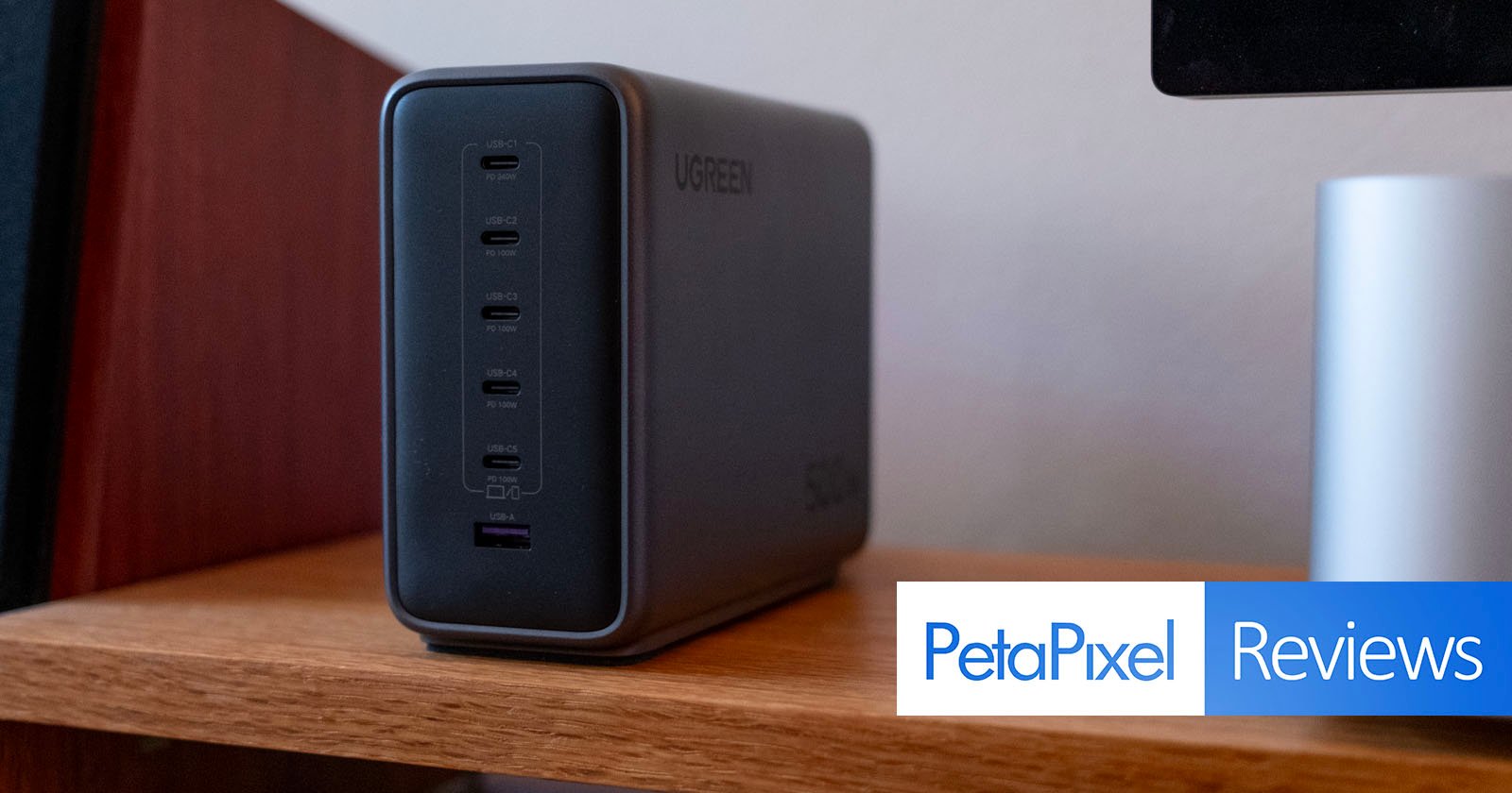 A UGREEN charging station with multiple USB-C and one USB-A port sits on a wooden shelf. The Petapixel Reviews logo appears in the bottom right corner. A UGREEN charging station with multiple USB-C and one USB-A port sits on a wooden shelf. The Petapixel Reviews logo appears in the bottom right corner.